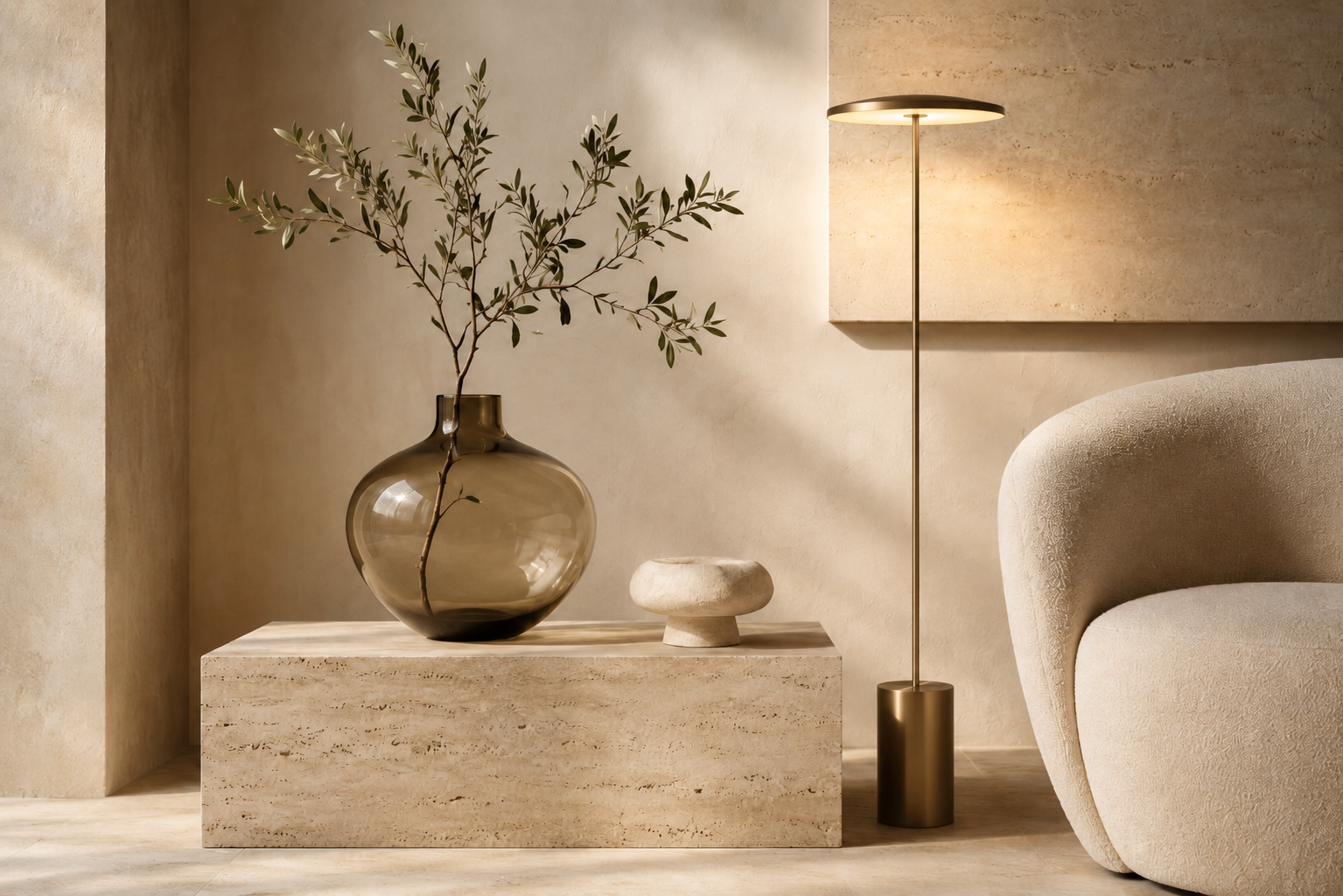 Warm minimal interior vignette with travertine plinth, glass vase and brass floor lamp